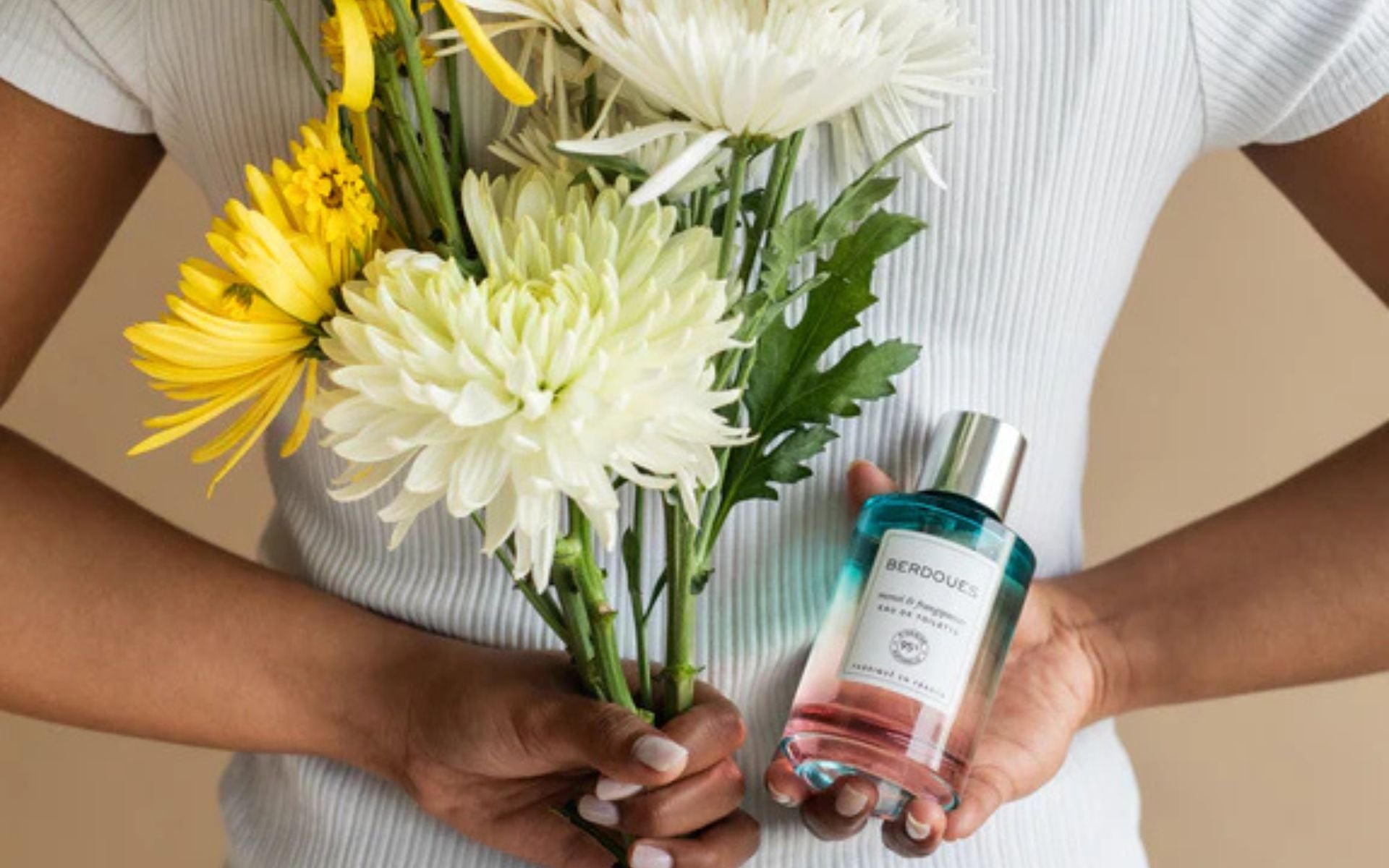Flacon de parfum Berdoues tenu dans la main aux côtés d’un bouquet de fleurs, illustrant une fragrance fraîche et florale.