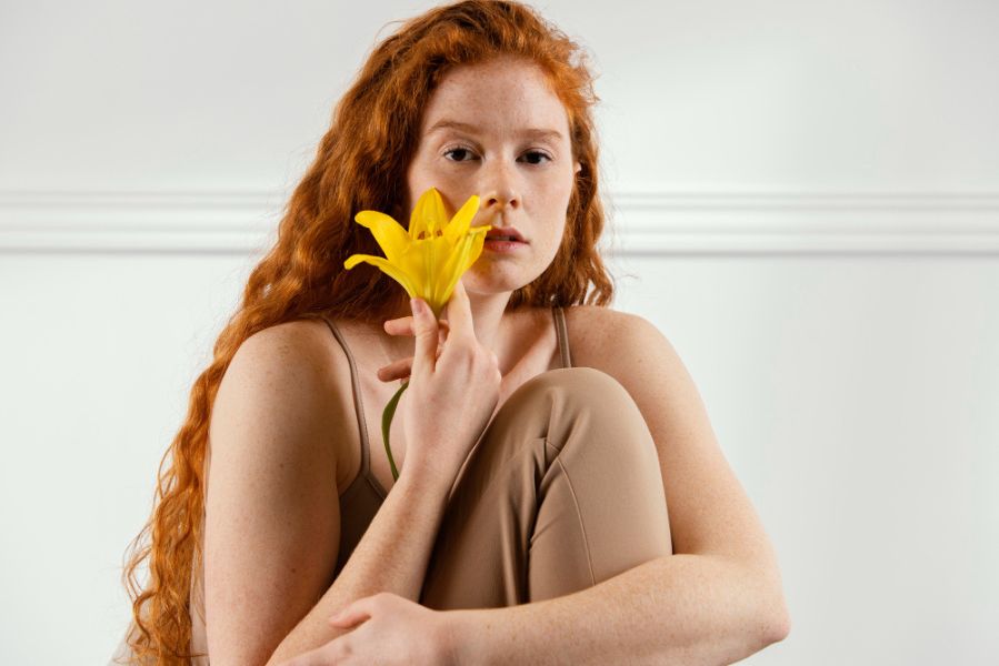 Femme rousse tenant une fleur jaune près du visage illustrant la sensibilité olfactive et la perception des parfums selon les périodes hormonales