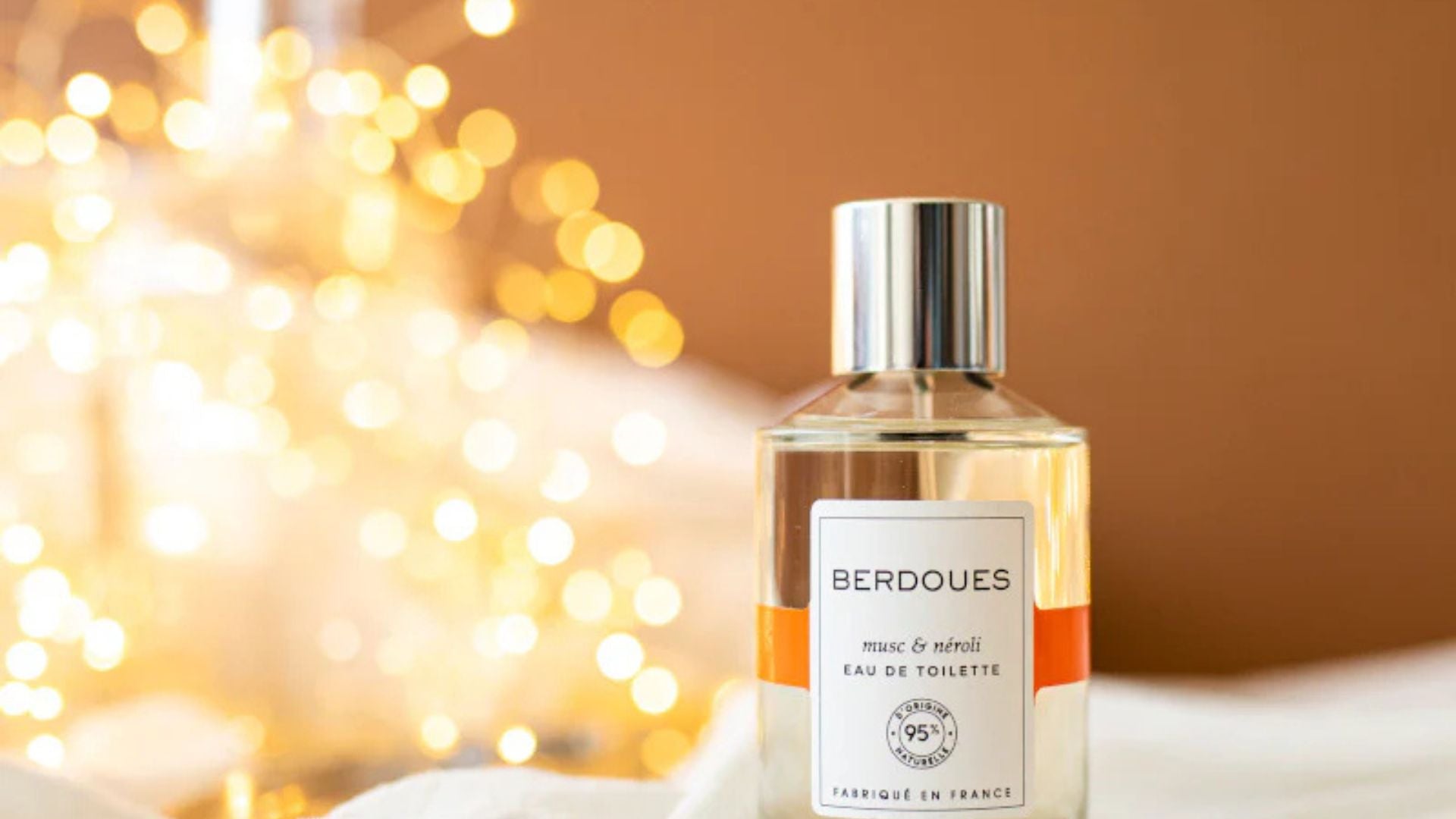 Un flacon d'eau de toilette Berdoues musc & néroli avec un design raffiné, posé sur un fond lumineux doré, représentant l'élégance et la subtilité des fragrances Berdoues.