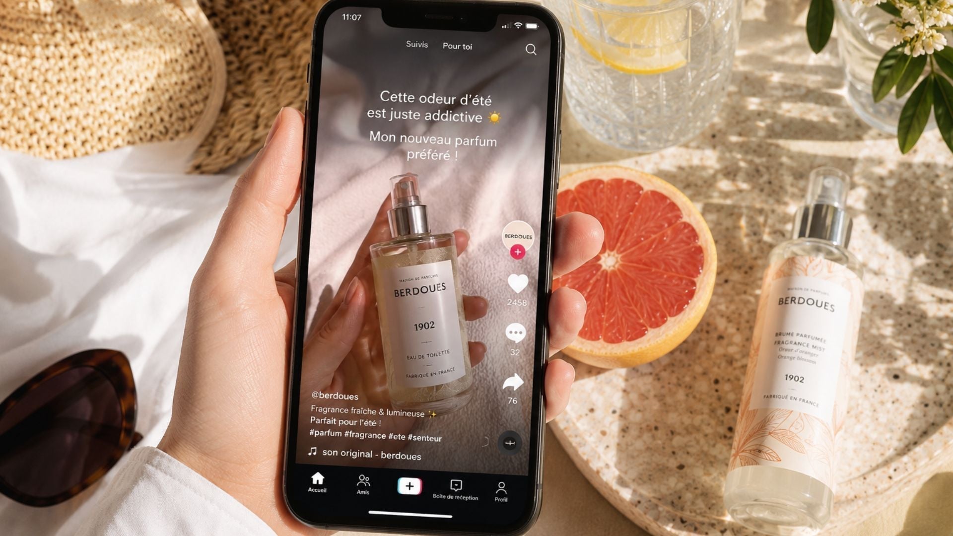 Smartphone affichant une vidéo de parfum tendance sur les réseaux sociaux à côté d'une brume parfumée Berdoues dans une ambiance estivale.